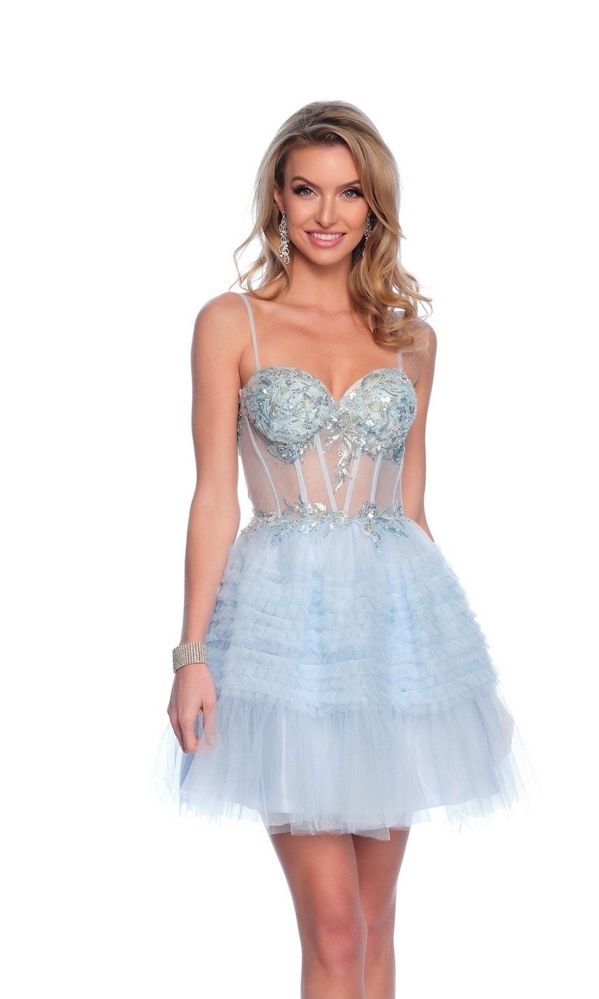 A woman poses and smiles in the Dave & Johnny Short Blue Ruffled Hoco Dress 11888, featuring an a-line tulle skirt, corset bodice, and delicate floral embellishments against a white background.